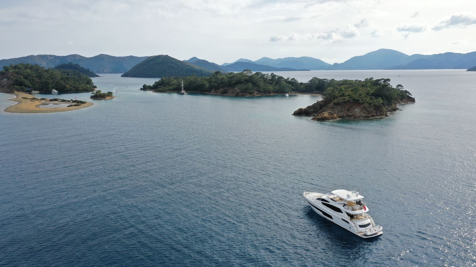 Göcek’in çamlarla kaplı adaları ve ön planda demirlemiş bir motoryat, havadan görünüm
